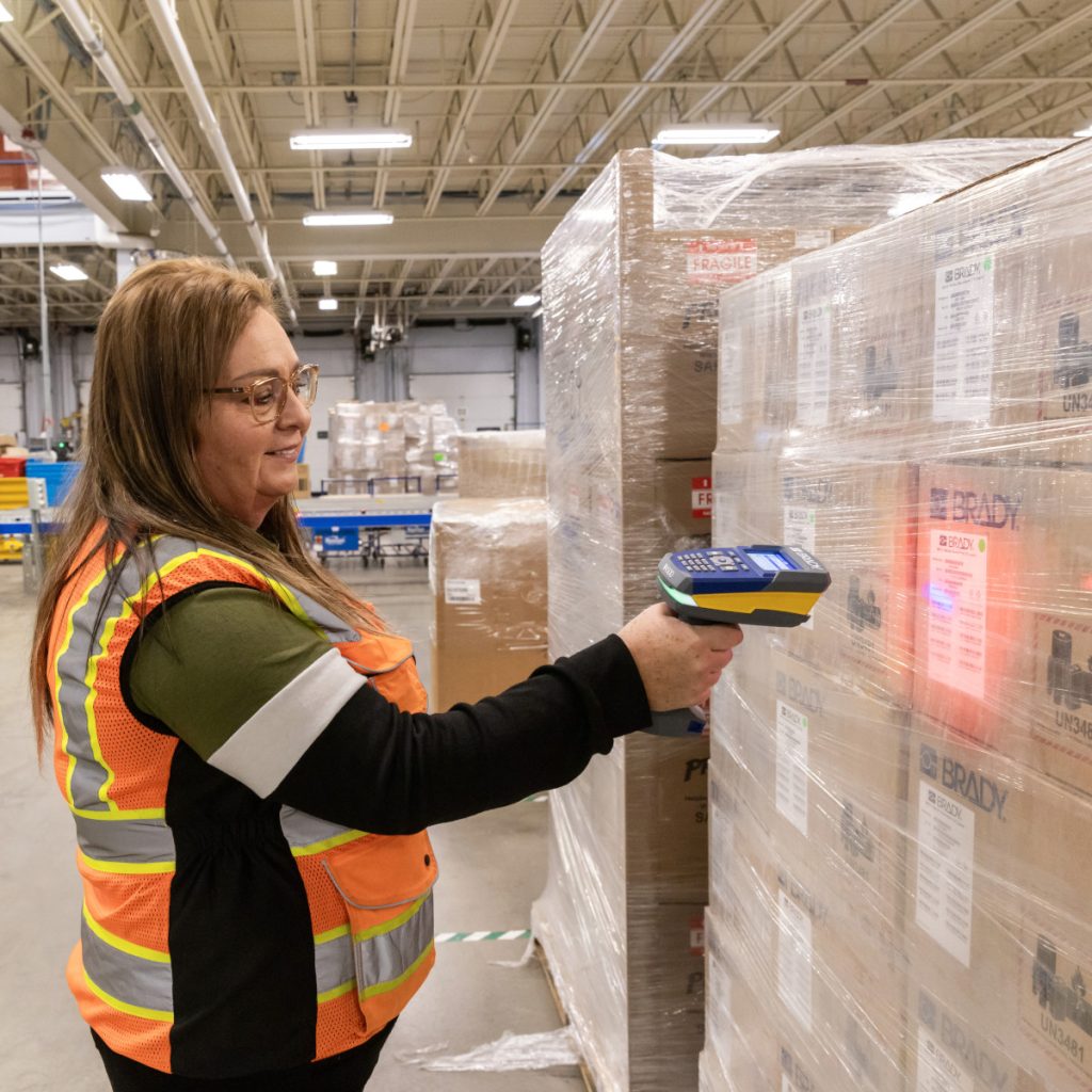 Woman in warehouse scanning barcode labels on boxes with Brady V4500 scanner.